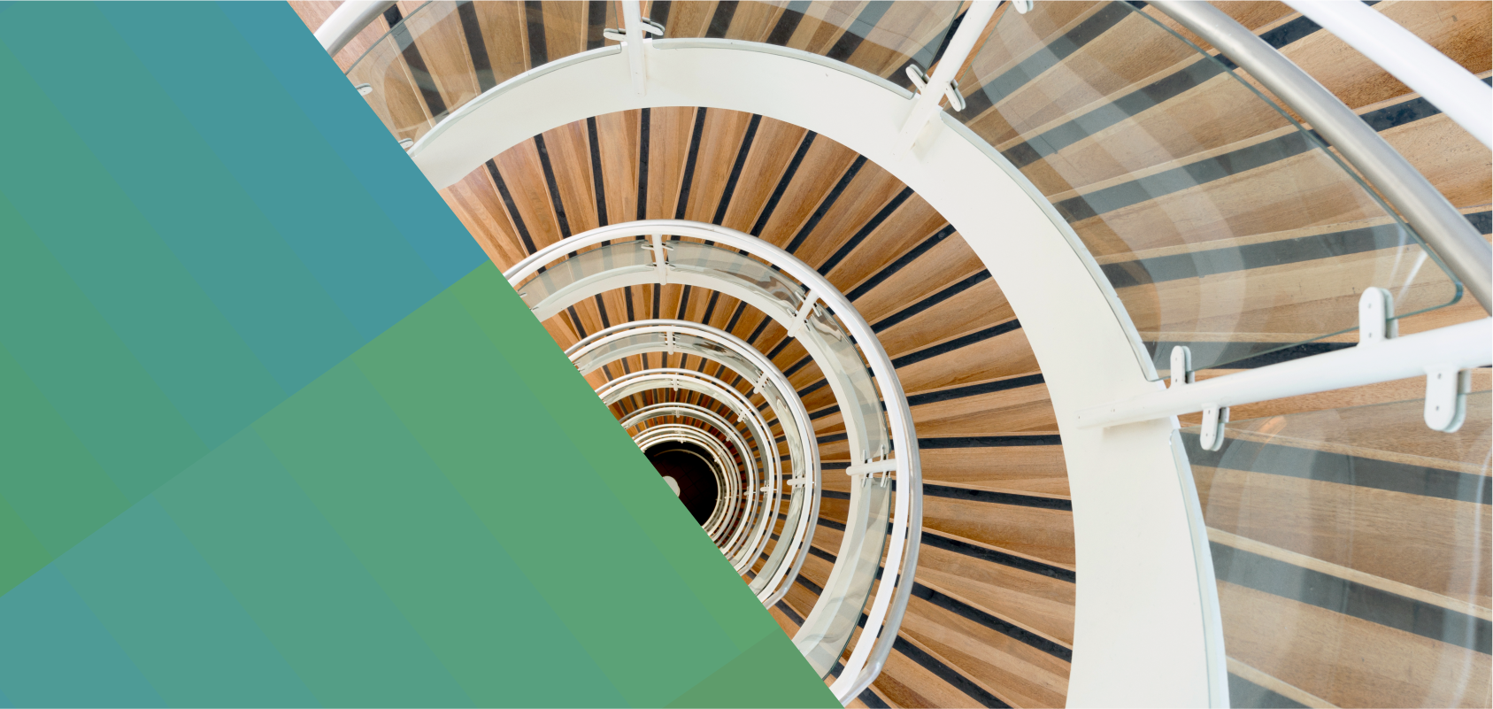 photo of a spiral staircase with glass railing and white metal barristers. The viewer is looking down from the top of the staircase so that the steps form a semi circle.