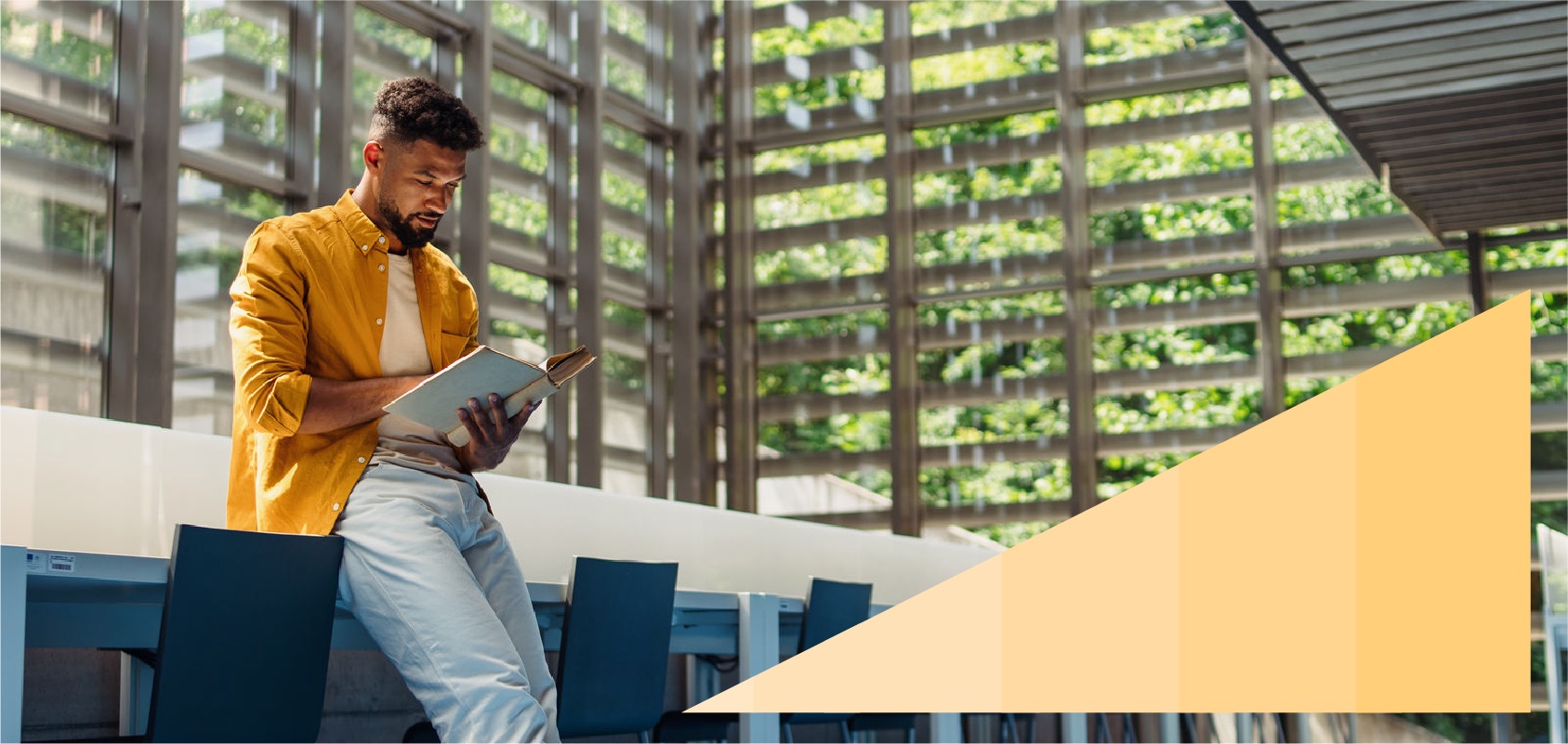 Young Black professional reading a book in a large naturally lit office lobby.